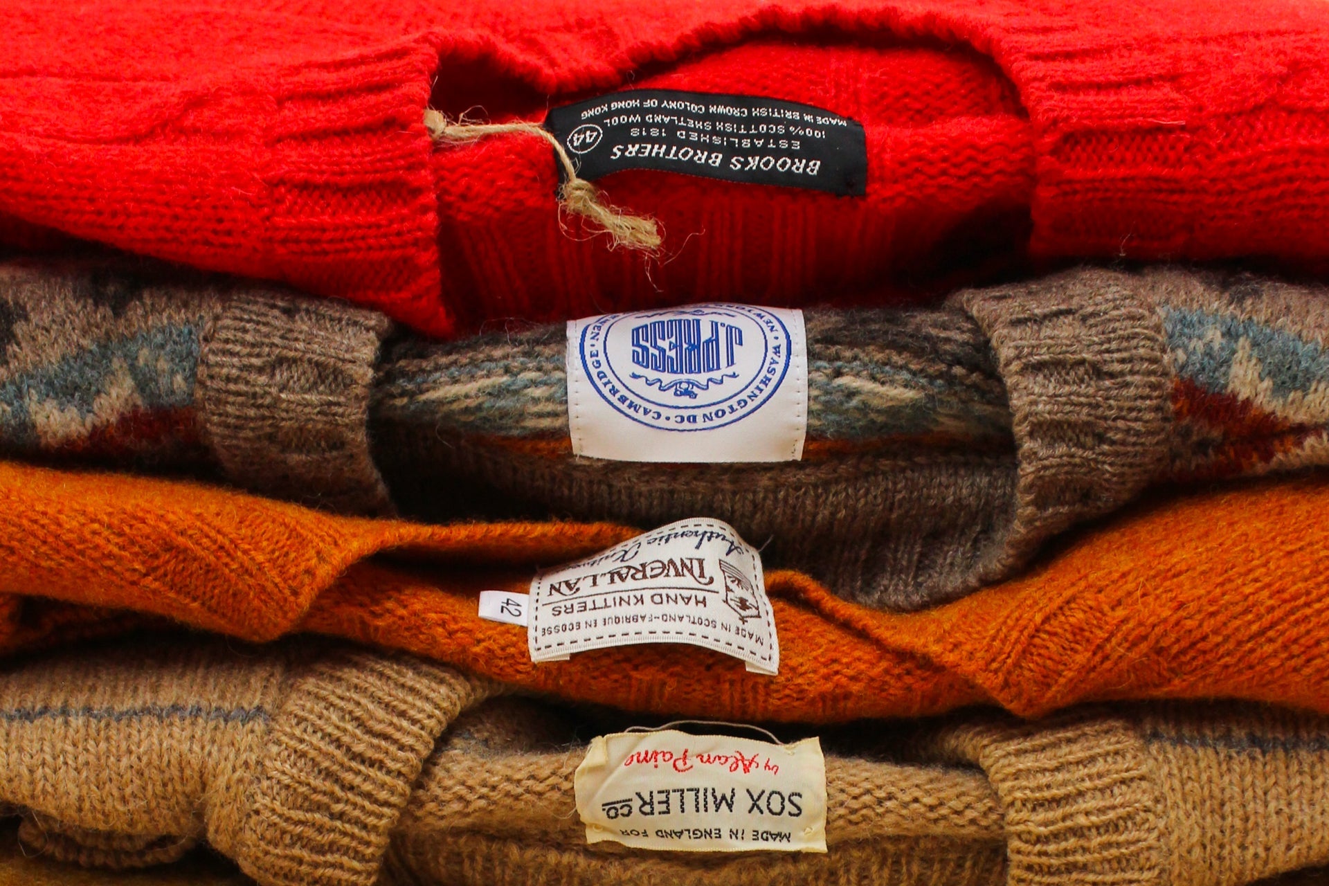 Stack of colorful sweaters with visible brand labels.